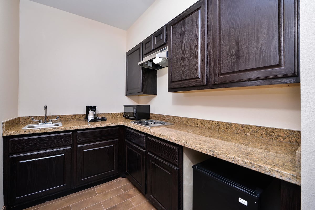 A compact kitchen with dark wood cabinets, a granite countertop, a built-in microwave, and a coffee maker.