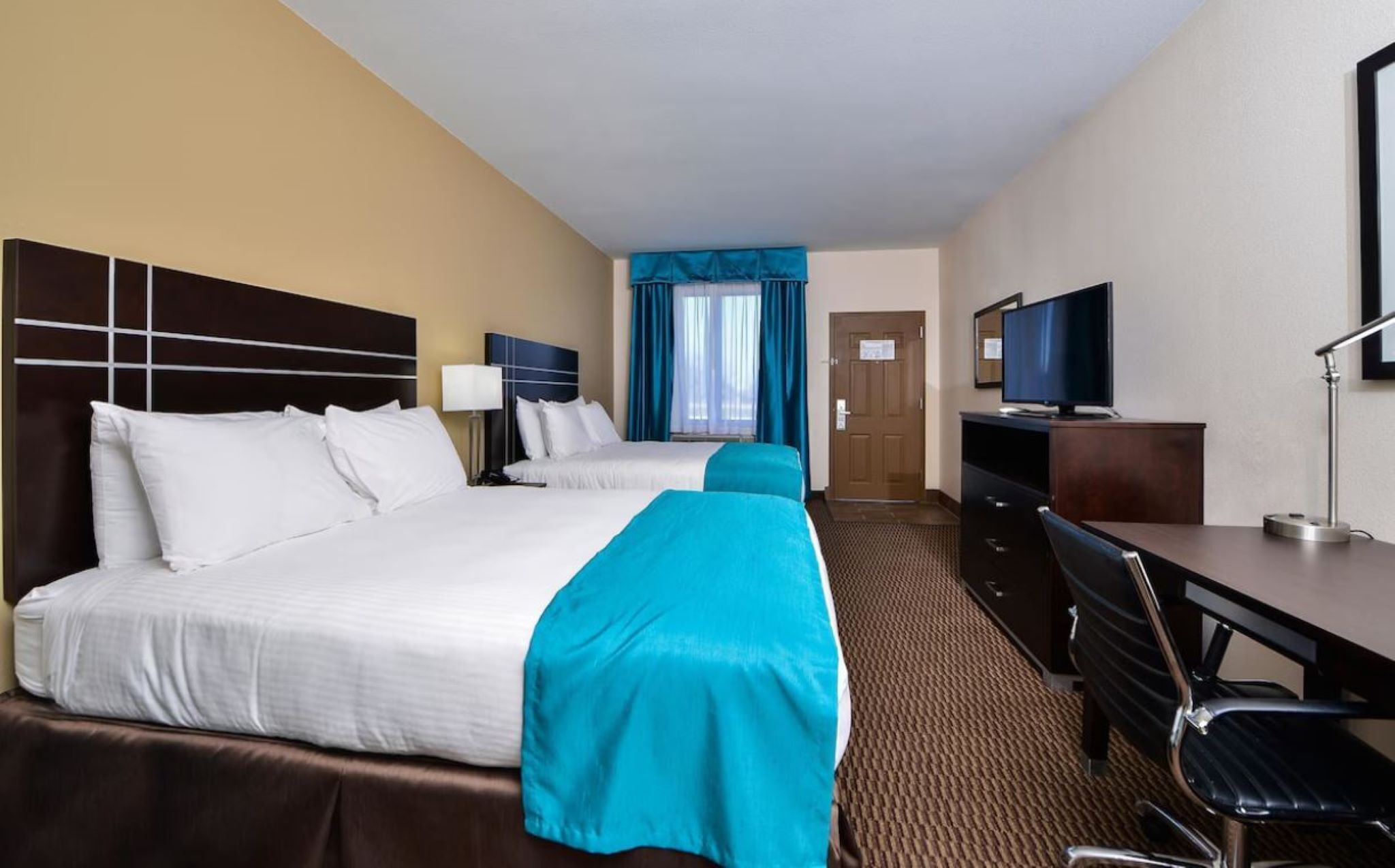 A hotel room with two beds, a desk, a television, and a chair.