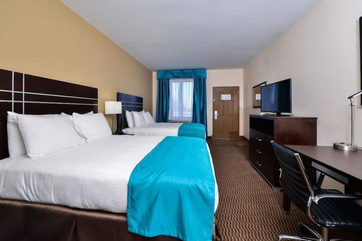 A hotel room with two beds, a desk, a television, and a chair.