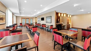 Een ruim restaurant met meerdere tafels en zitjes, uitgevoerd in een modern design met rode en zwarte stoelen.