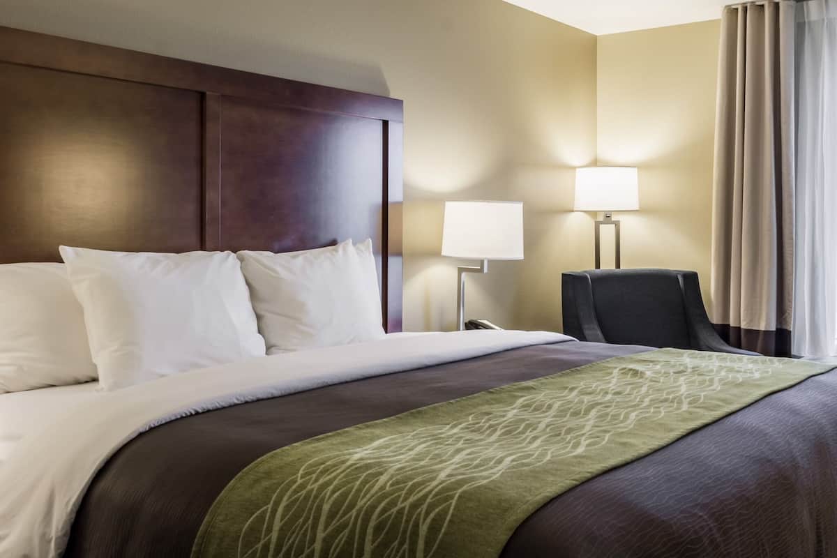A hotel room with a large bed, a headboard, a bedside table with a lamp, and a chair.