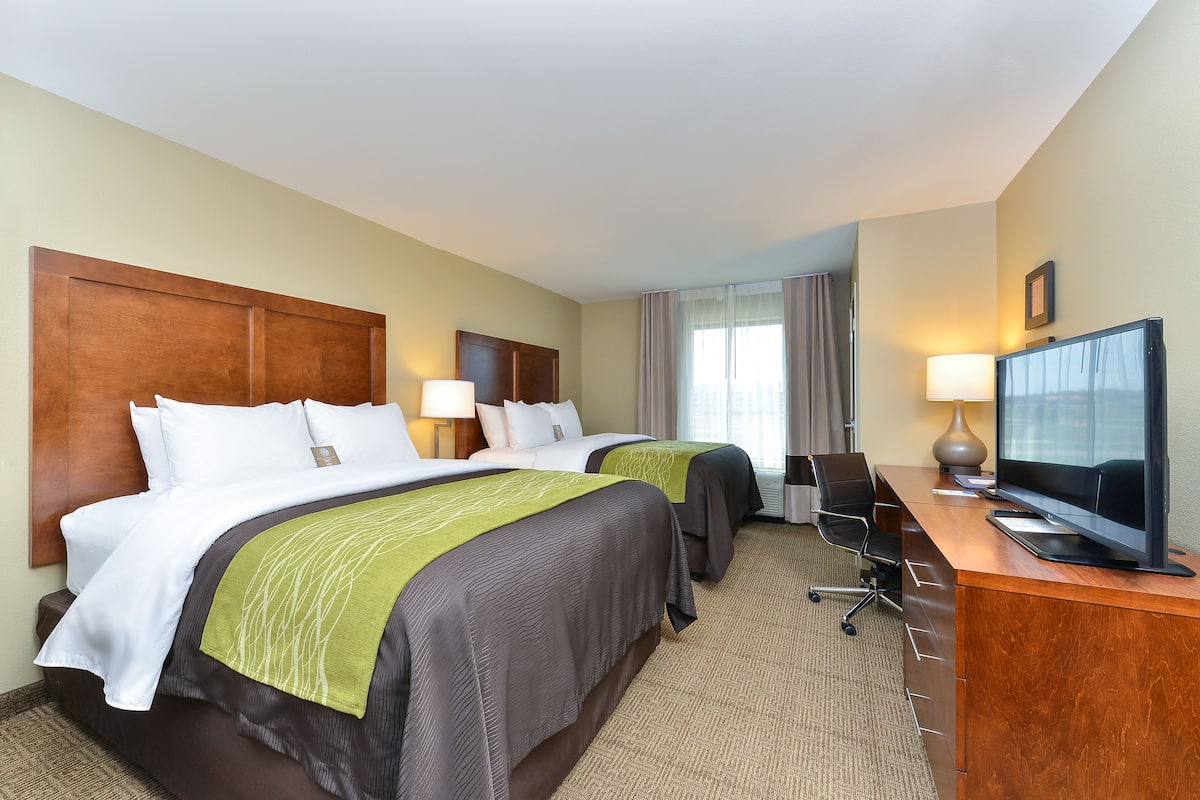 A hotel room with two beds, a desk with a television, and a chair.