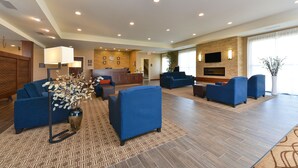 Een hotel lobby met blauwe banken, een receptiebalie, een open haard en een aan de muur bevestigde televisie.