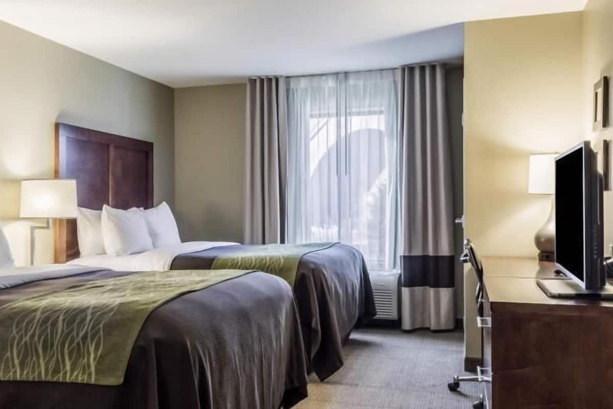 A hotel room with two beds, a TV, a desk, and a window with curtains.