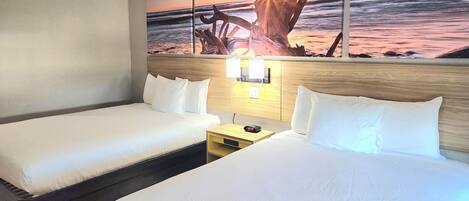 A hotel room with two beds, a nightstand, a wall-mounted lamp, and a painting of a sunset over the ocean.