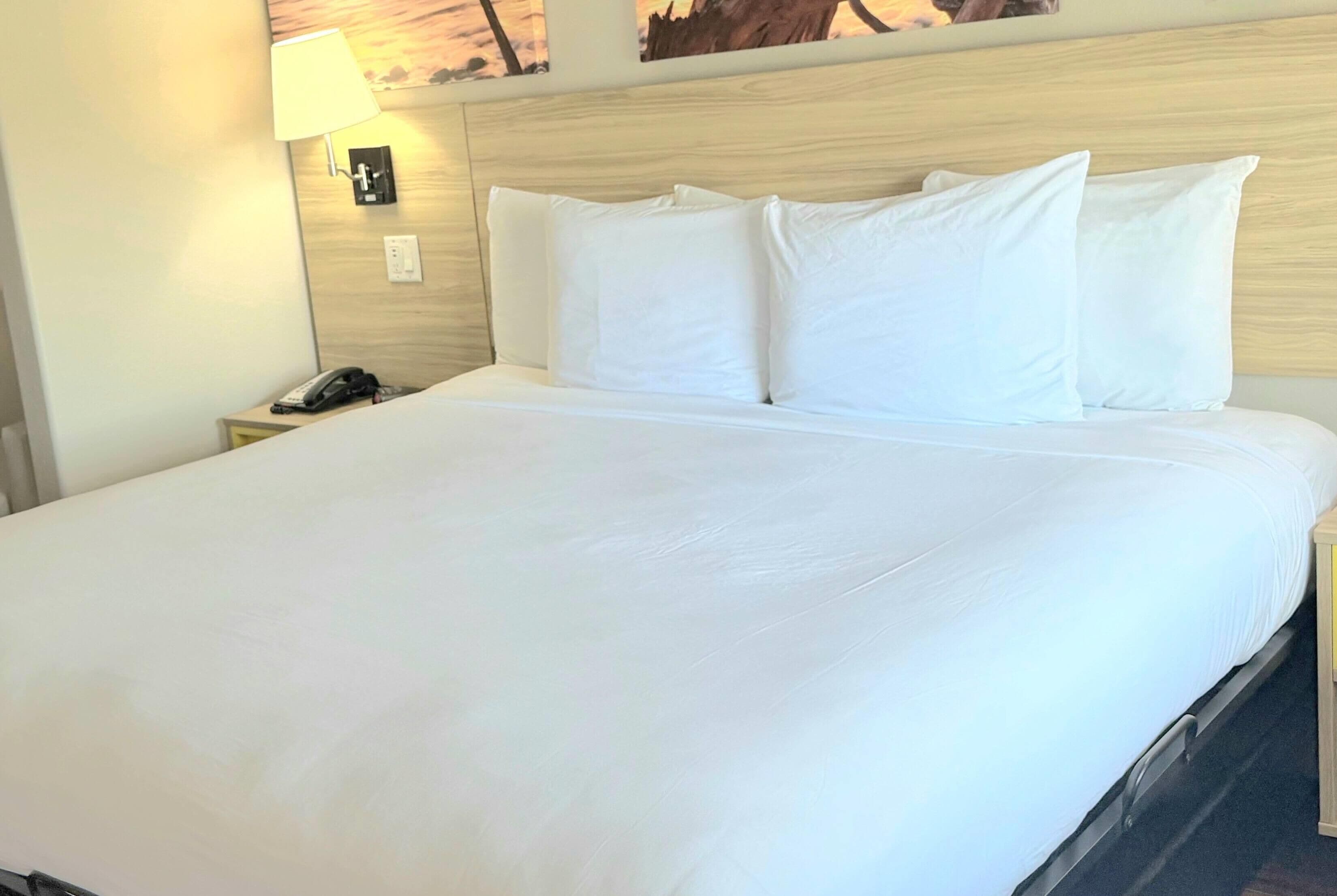Una camera d'albergo con un letto grande, una lampada da comodino, un telefono sul tavolino e un interruttore della luce fissato al muro.