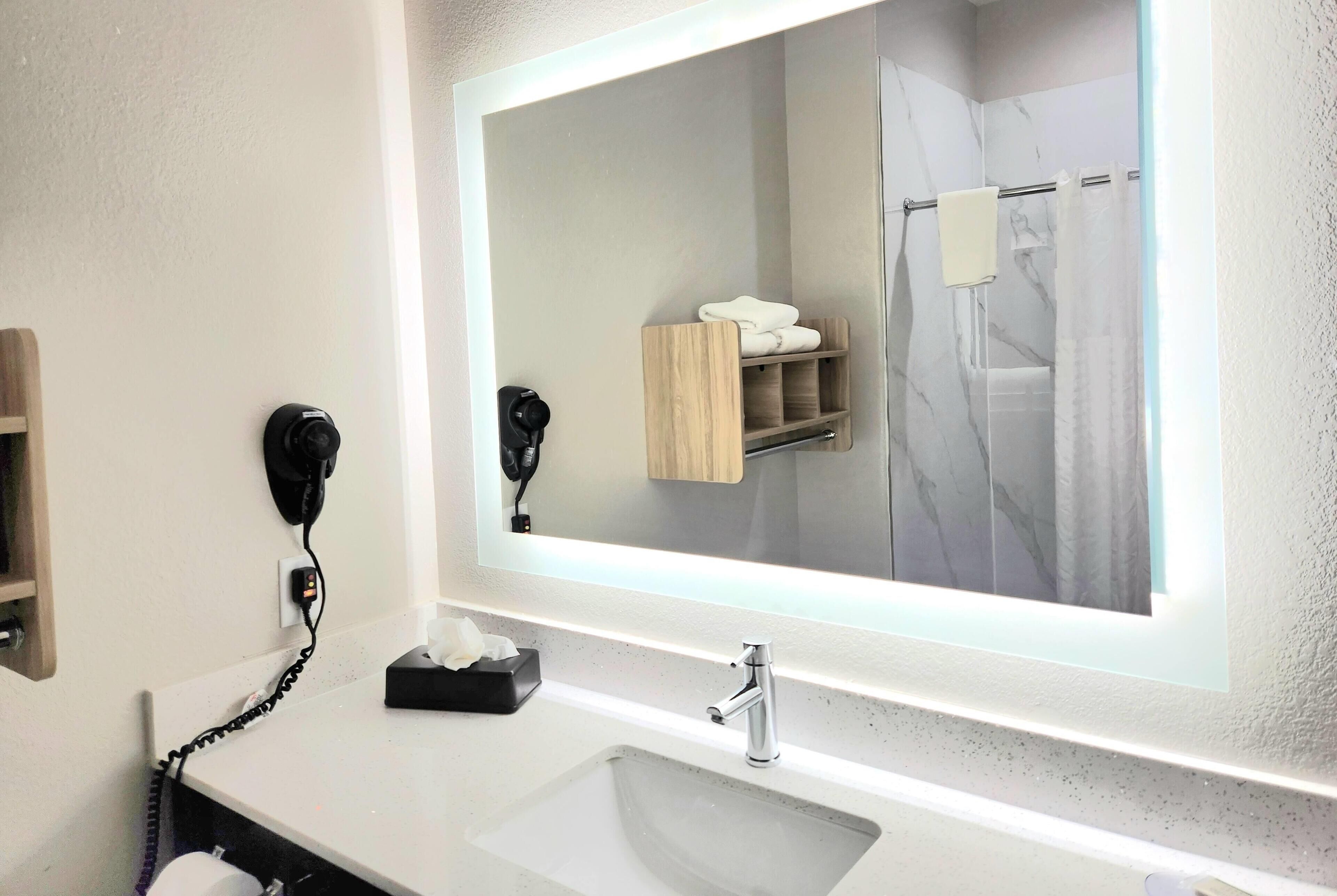 Une salle de bain avec un grand miroir, un lavabo, un sèche-cheveux et un porte-serviettes.
