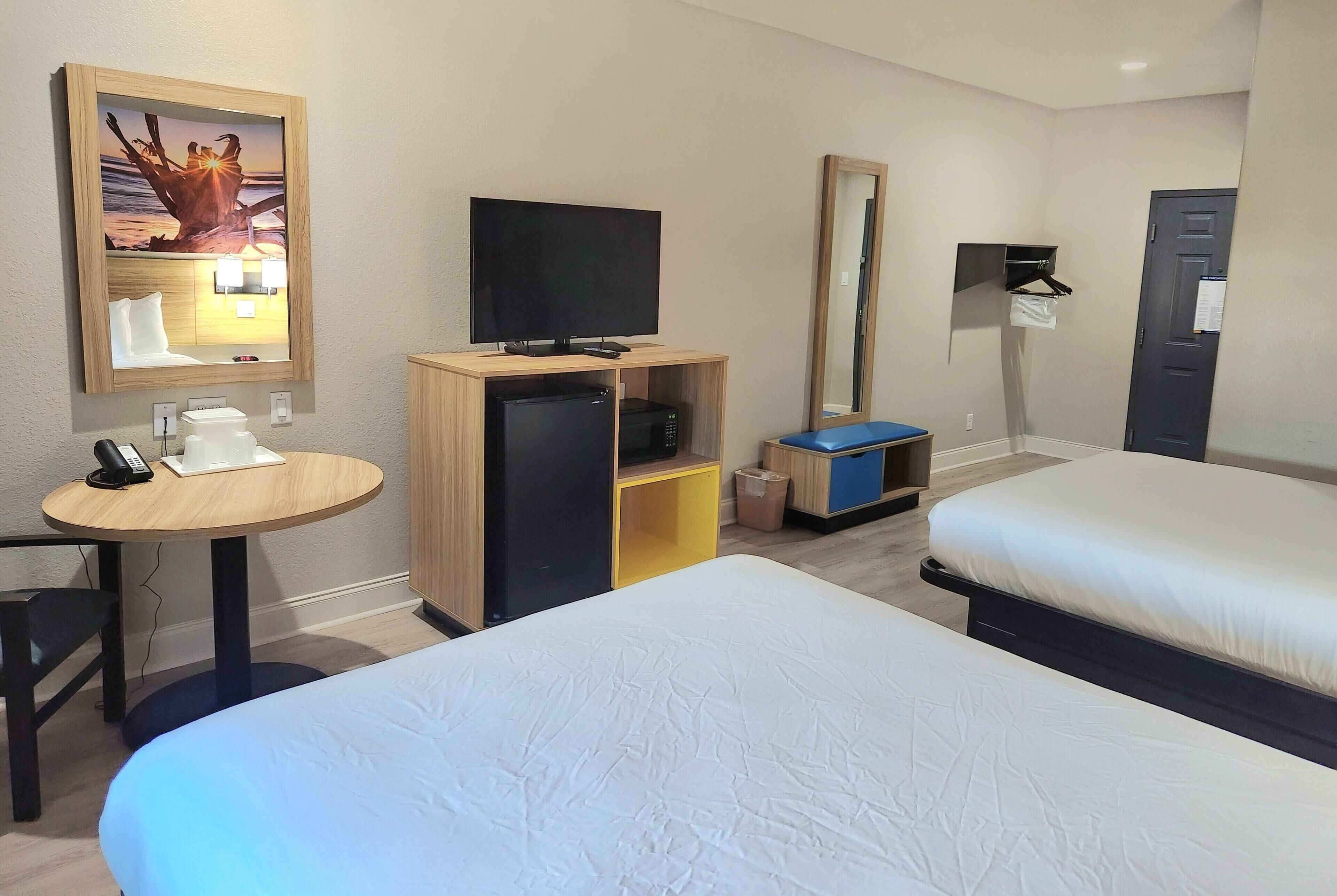 Habitación de hotel con dos camas, un escritorio con teléfono, televisión y un refrigerador pequeño.