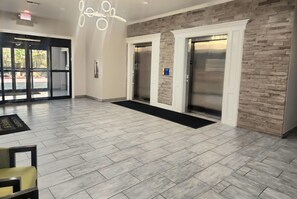 A lobby with a herringbone-patterned floor, a modern chandelier, and two elevators.