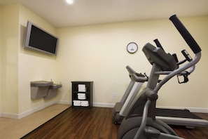 A home gym with a treadmill, a stationary bike, and a wall-mounted TV. - Days Inn & Suites by Wyndham Galveston West/Seawall (Galveston)