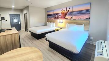 A hotel room with two beds, a desk, a chair, and a painting of a sunset.