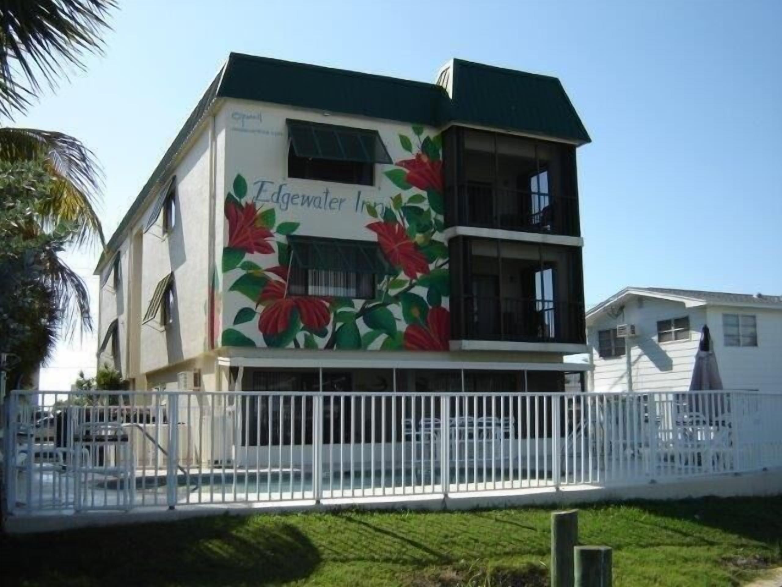 A two-story building with a green roof and a mural of red flowers on the side.