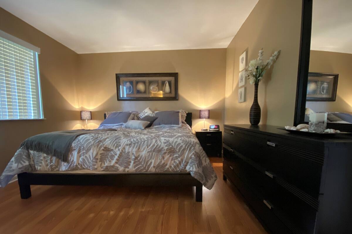 Une chambre à coucher comprenant un lit, des tables de chevet, une commode et un grand miroir.