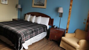 A bedroom with a bed, bedside table, lamp, and a chair. - Wyatt Earp Hotel (Dodge City)
