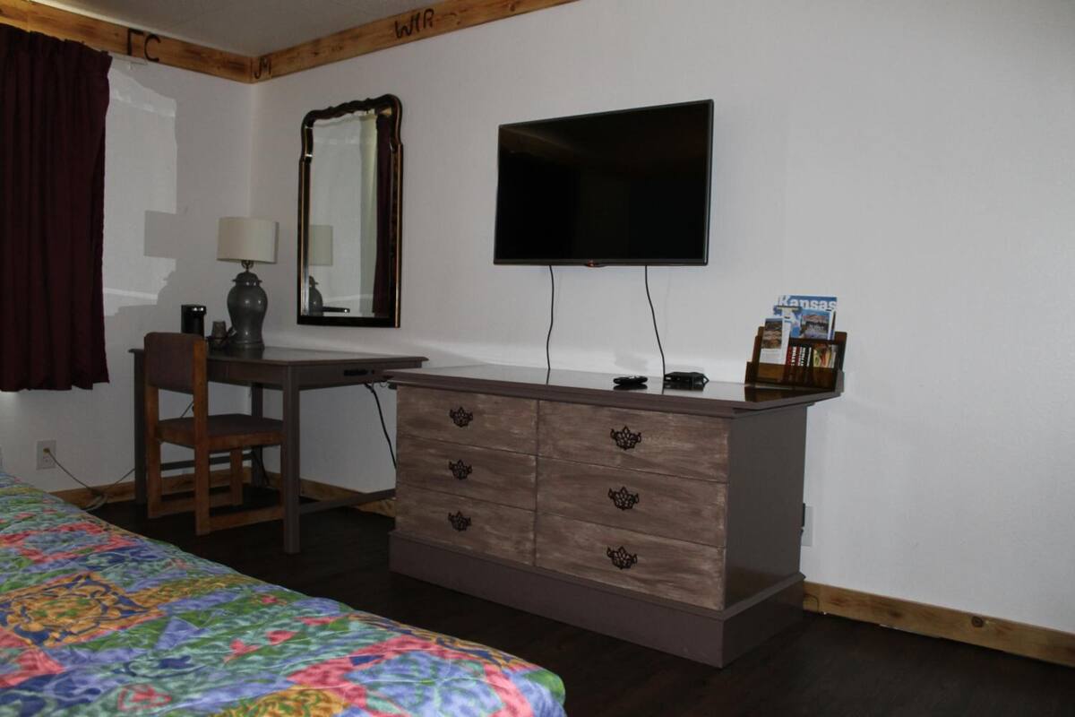 Ein Schlafzimmer mit Bett, Schreibtisch, Stuhl, Kommode, Fernseher und Spiegel.