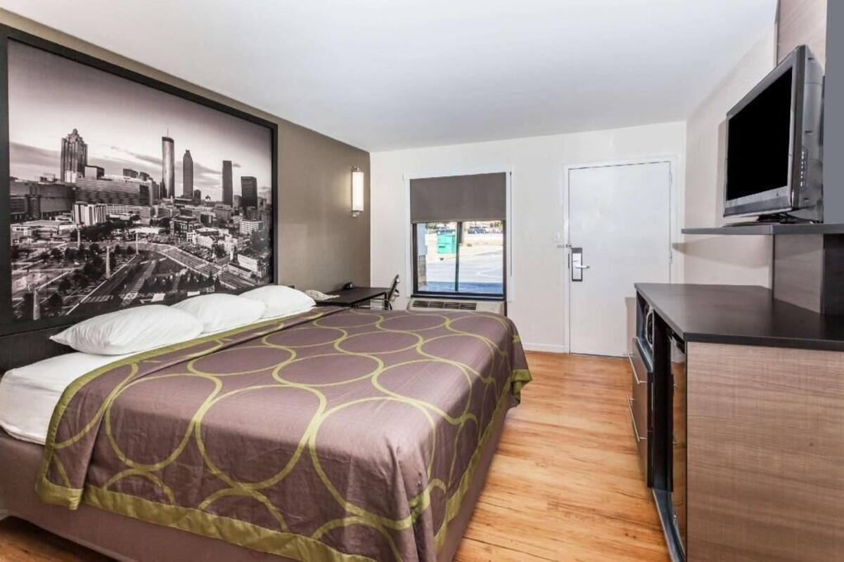 A hotel room with a bed, a television, a window, and a cityscape mural.