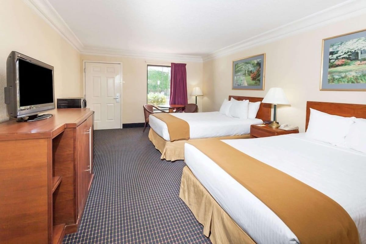 Habitación de hotel con dos camas, televisión, escritorio y ventana con cortinas.