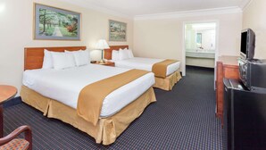 A hotel room with two beds, a desk, a television, and artwork on the walls.