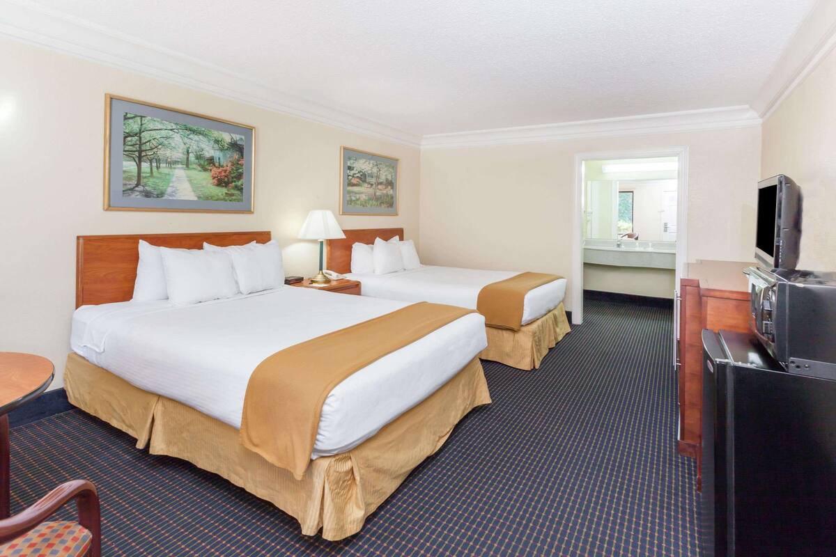 A hotel room with two beds, a desk, a television, and artwork on the walls.