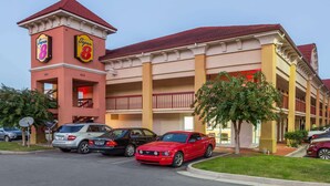 A hotel with a red and beige facade, multiple balconies, and a parking lot with several cars.