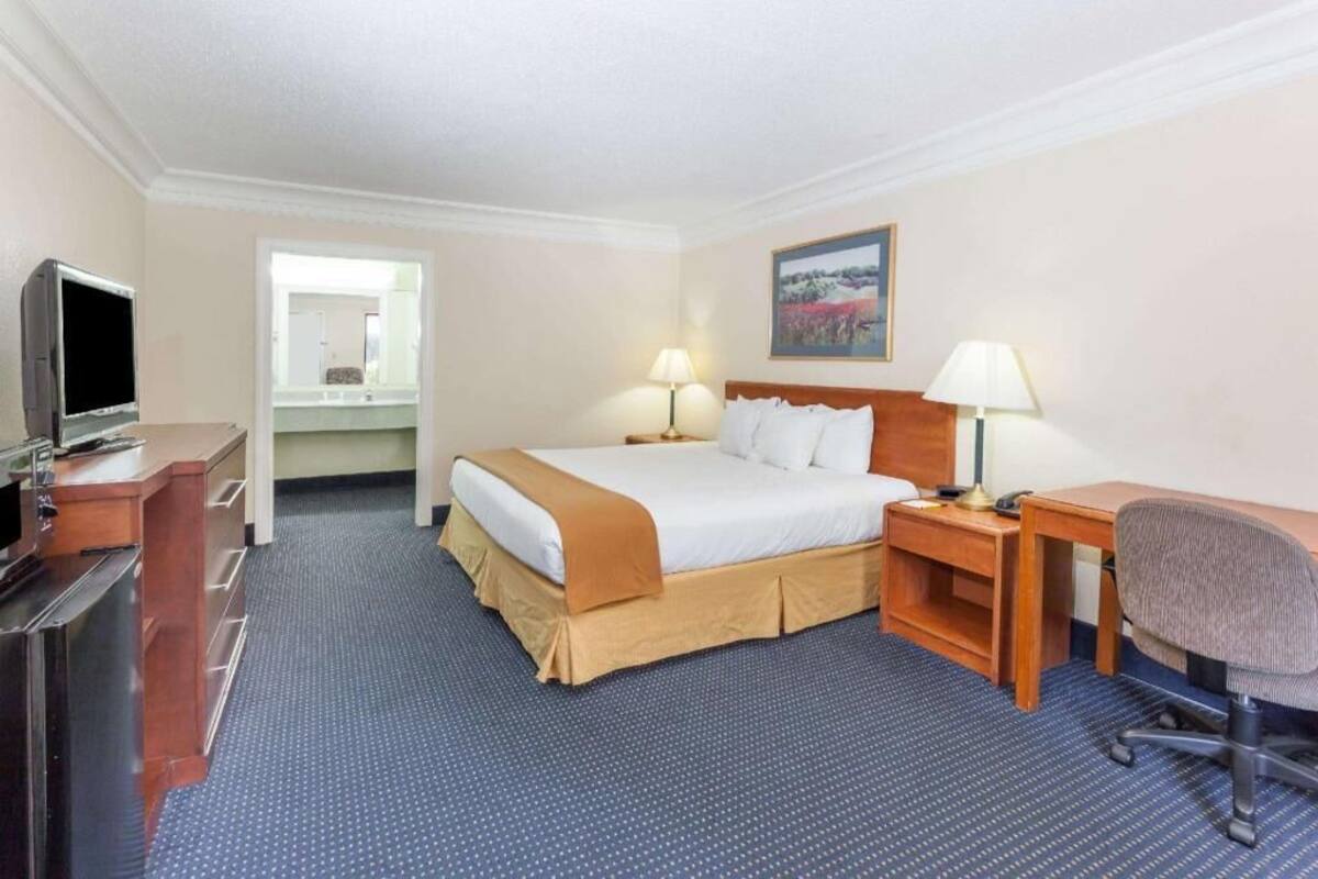A hotel room with a bed, desk, chair, TV, and a bathroom visible through an open door.