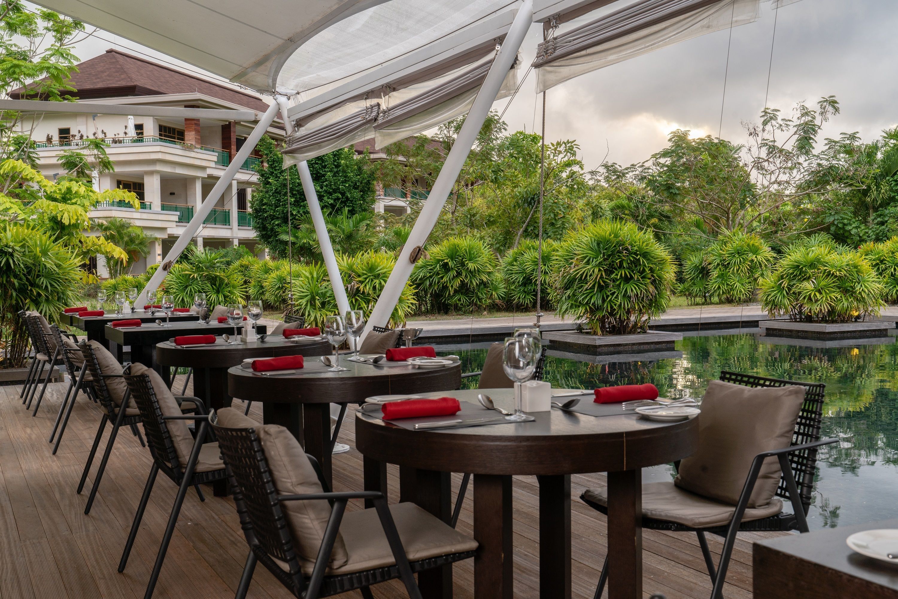 An outdoor dining area with tables and chairs, a pool, and lush greenery.