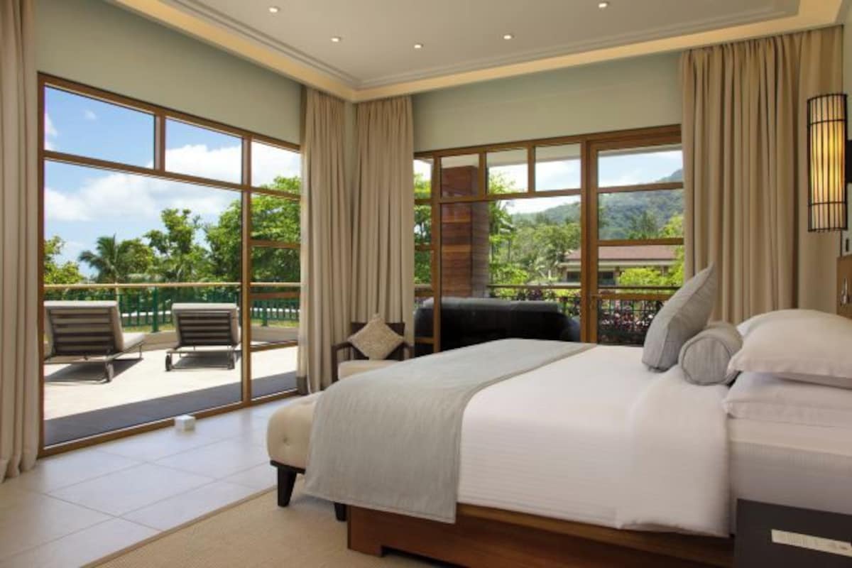 A bedroom with a large bed, a view of the outdoors, and a balcony with chairs.