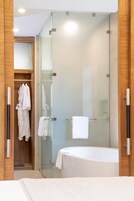 Un baño moderno con ducha de vidrio, vestidor y una bañera grande.