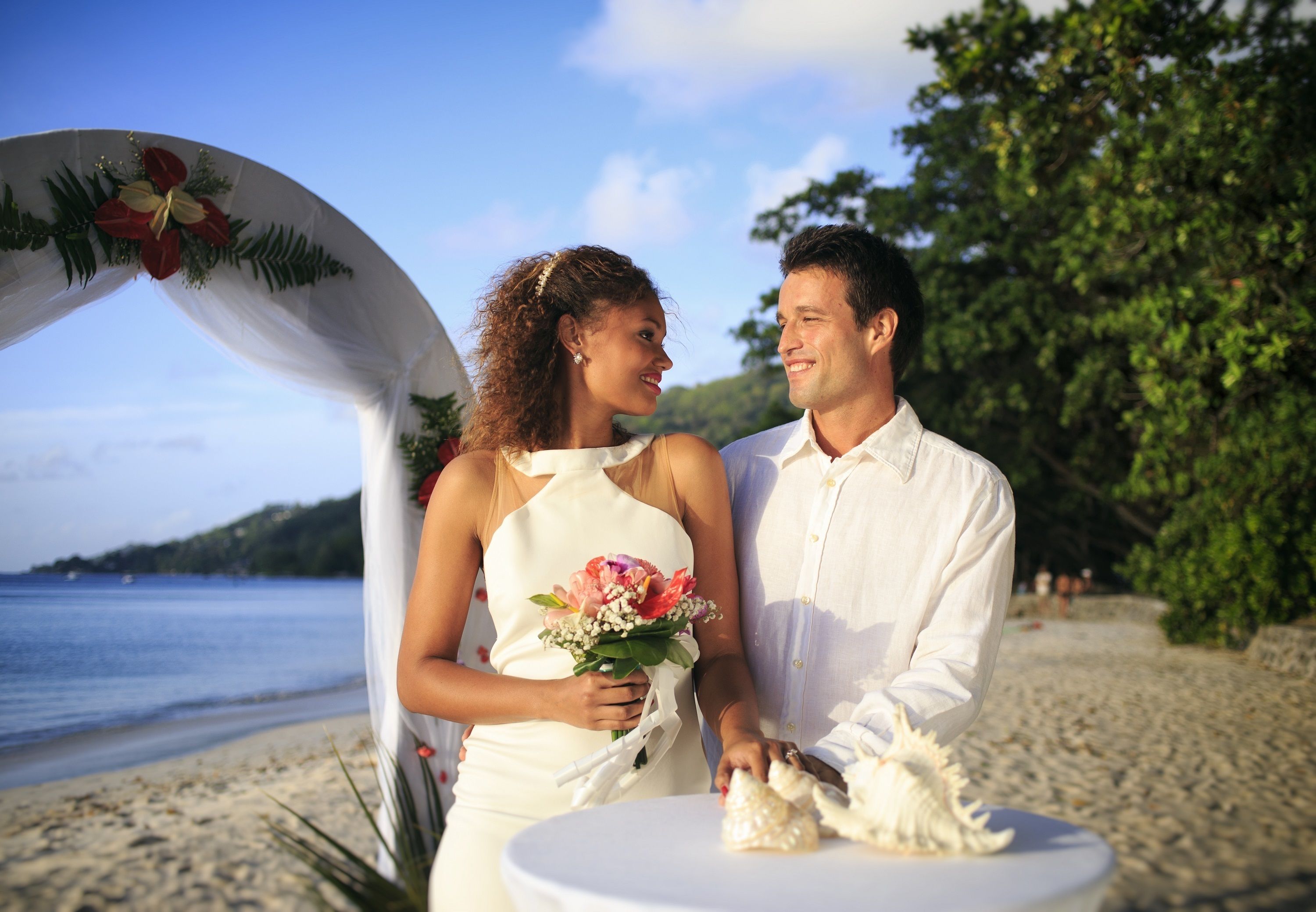 Decoración para una boda en la playa, con un arco blanco y adornos florales.