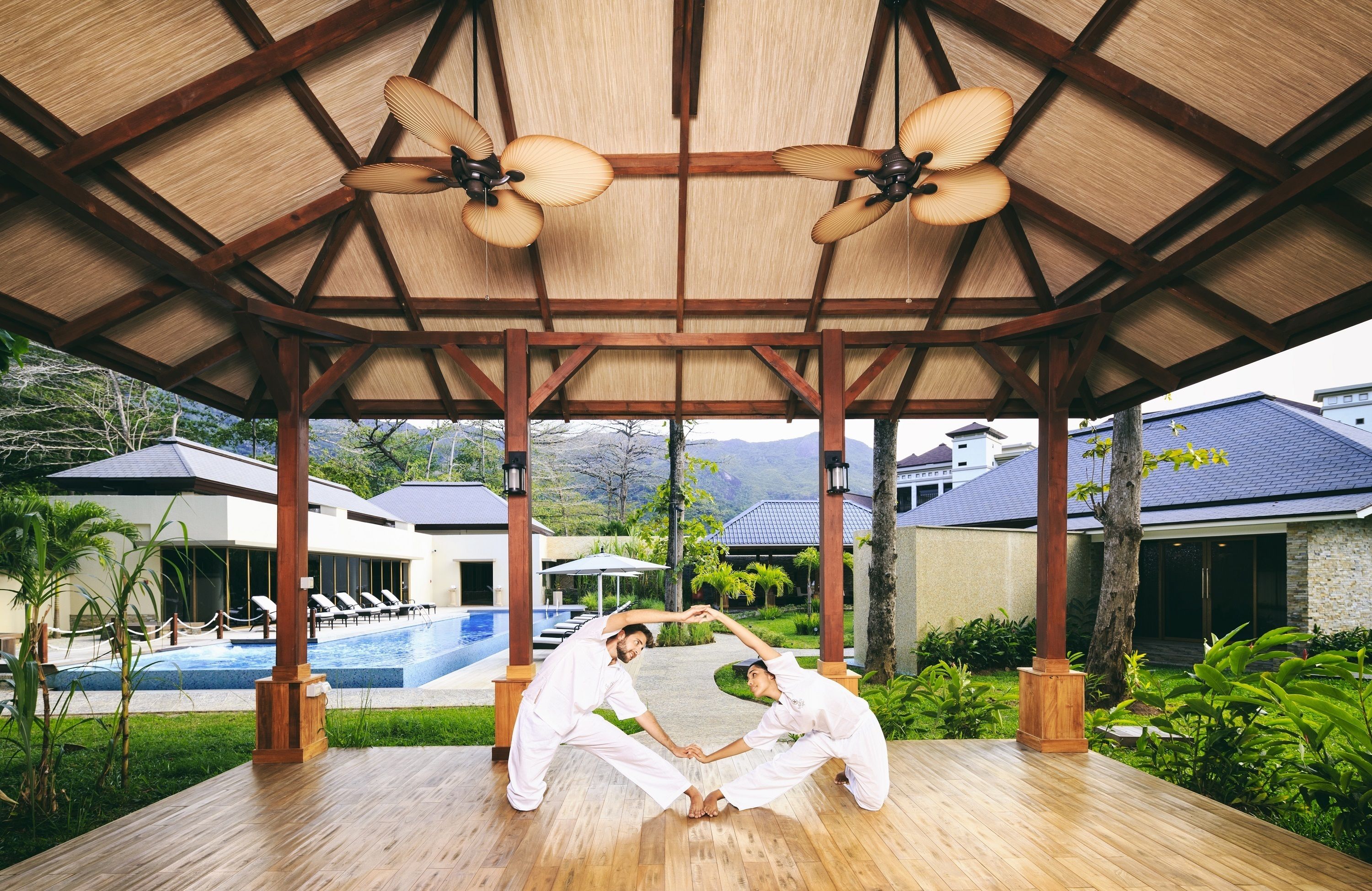 Un espacio al aire libre cubierto con piscina, terraza de madera y ventiladores de techo.