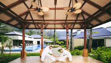 Un espacio al aire libre cubierto con piscina, terraza de madera y ventiladores de techo.