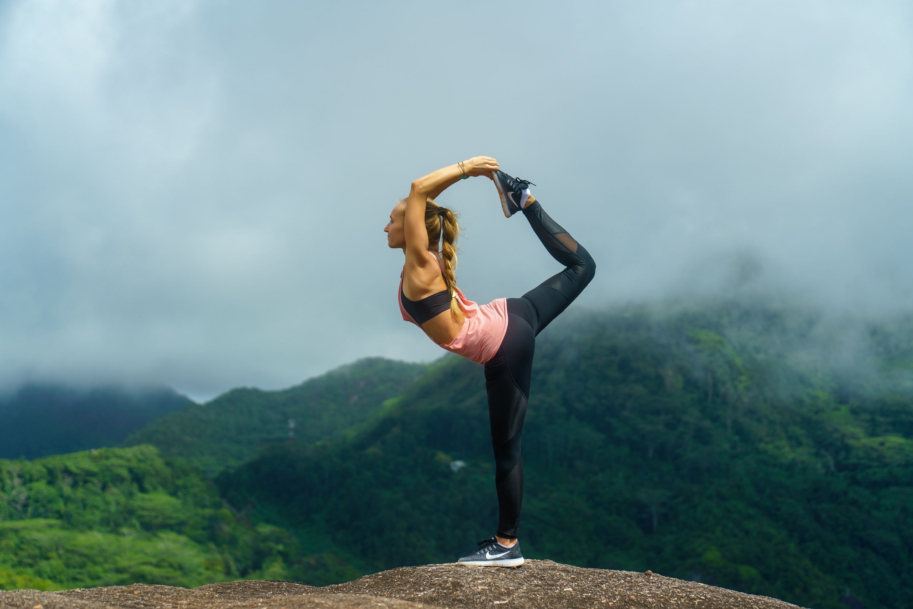 Una persona realizando una postura de yoga sobre un saliente rocoso, con montañas al fondo.