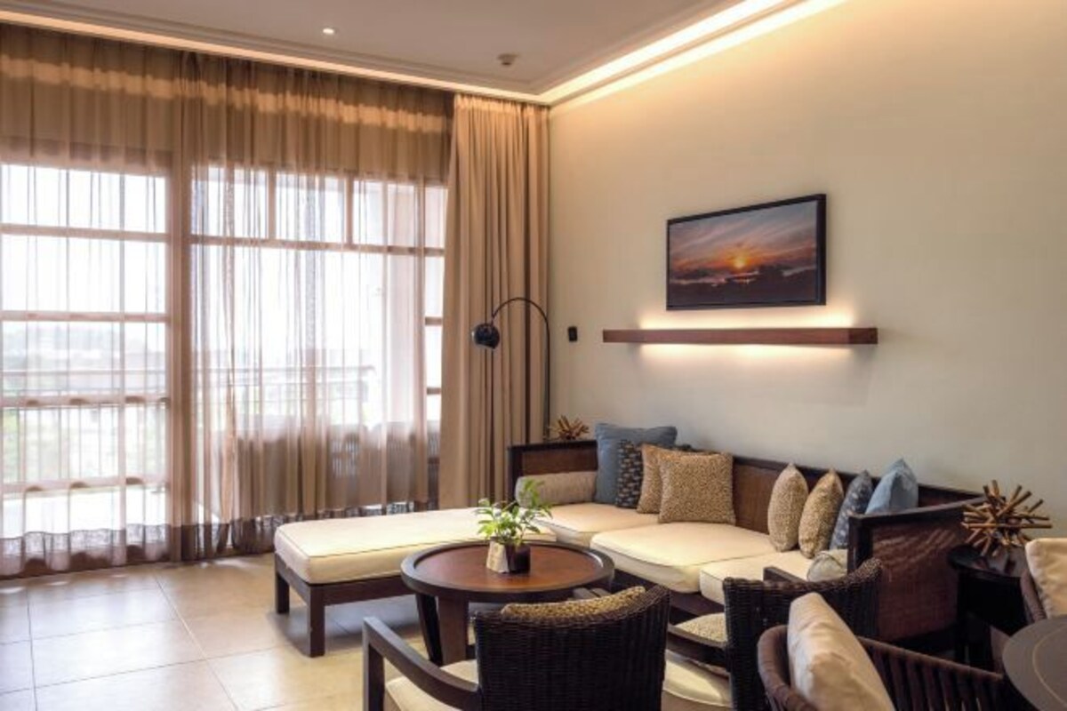 A modern living room with a sofa, a coffee table, and a large window with curtains.