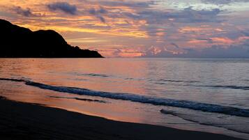 A beach with waves at sunset, a silhouette of a mountain, and a clear sky.