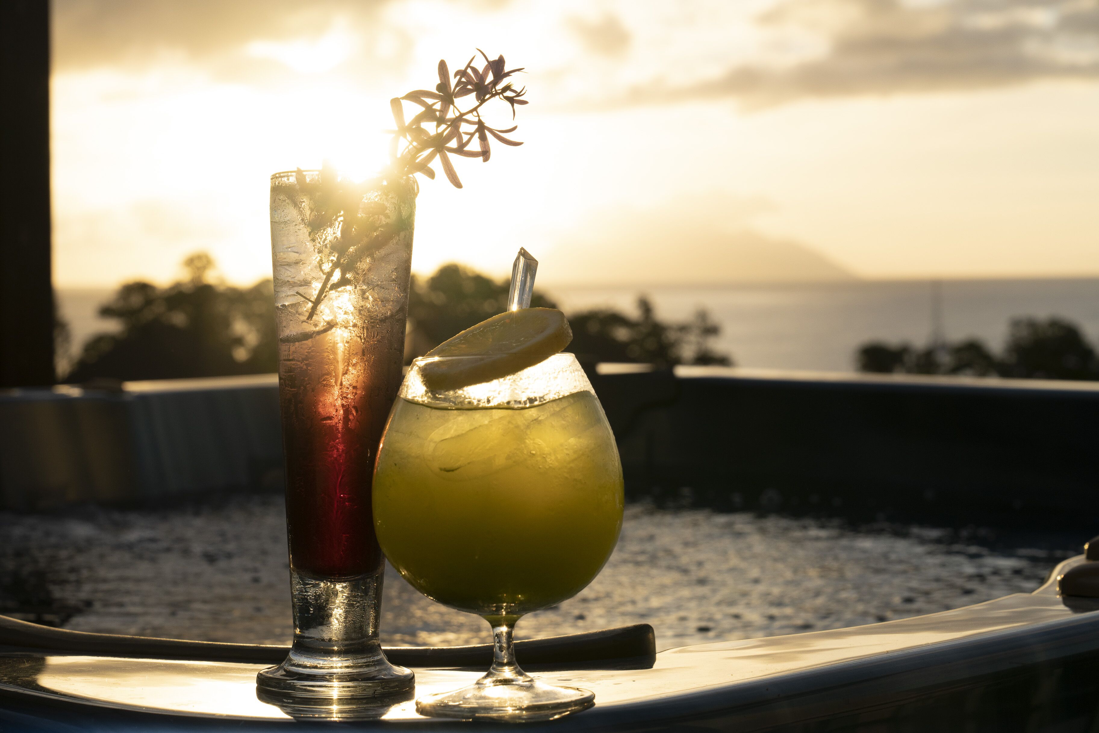 Two drinks on a tray with a scenic view of the ocean and mountains in the background.