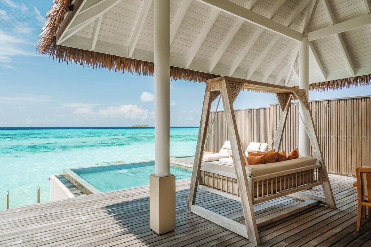 A wooden deck with a swing chair overlooking a clear blue sea.