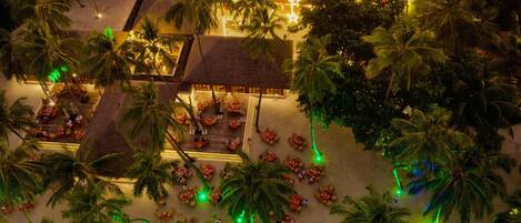 An aerial view of a resort with thatched-roof structures, palm trees, and outdoor seating areas.