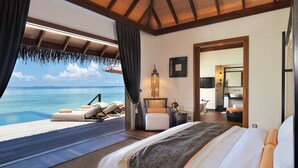 A bedroom with a large bed, a view of the ocean, a sitting area with a chair and a table, and a bathroom visible through an open door. - Ayada Maldives (Maguhdhuvaa)