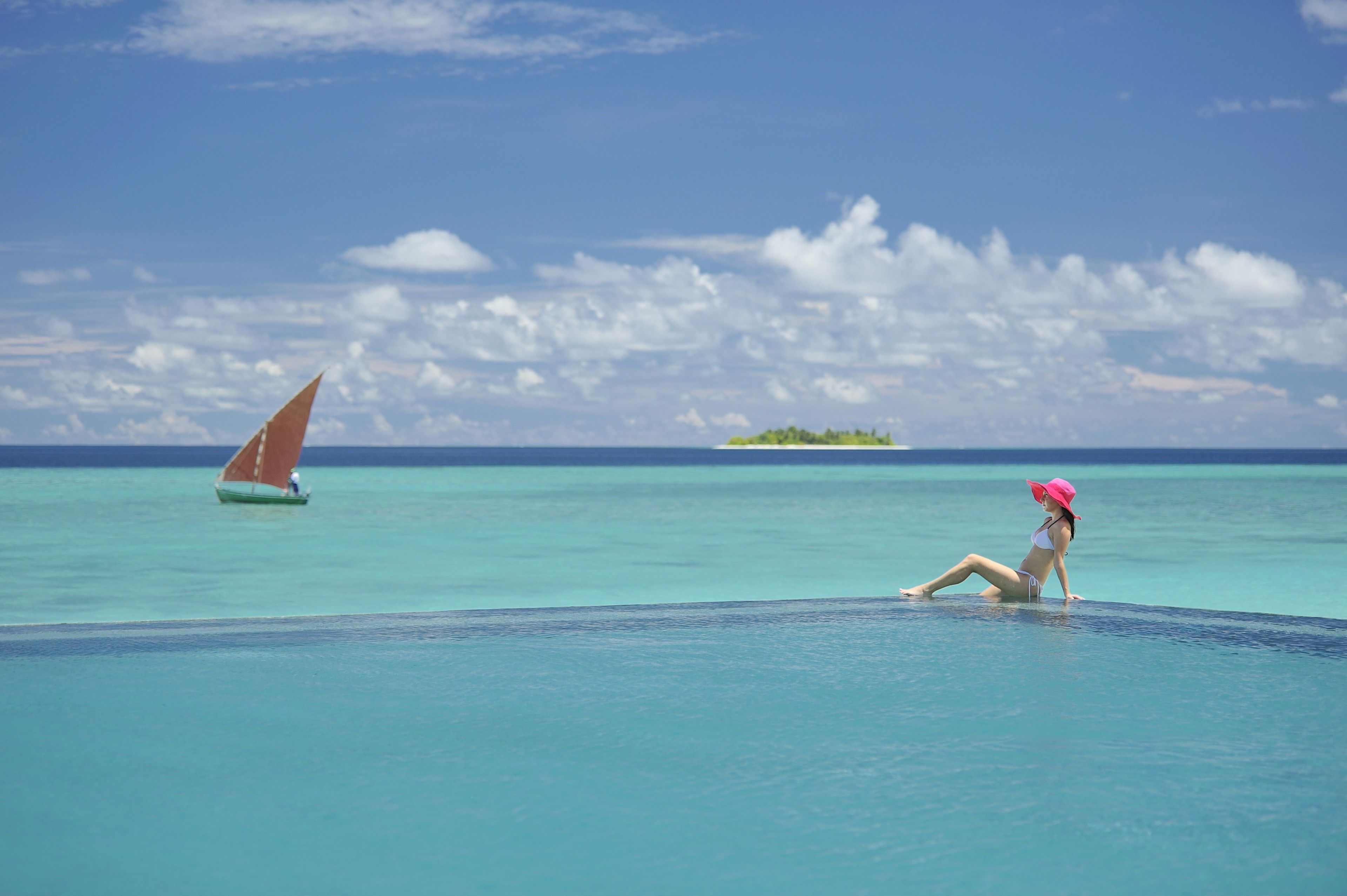 A woman sitting by a pool with a sailboat in the background.