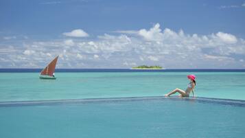 A woman sitting by a pool with a sailboat in the background.