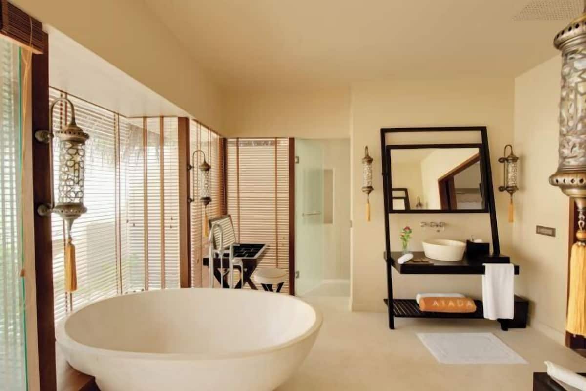 A bathroom with a large bathtub, a mirror, a sink, and a shelf with toiletries.