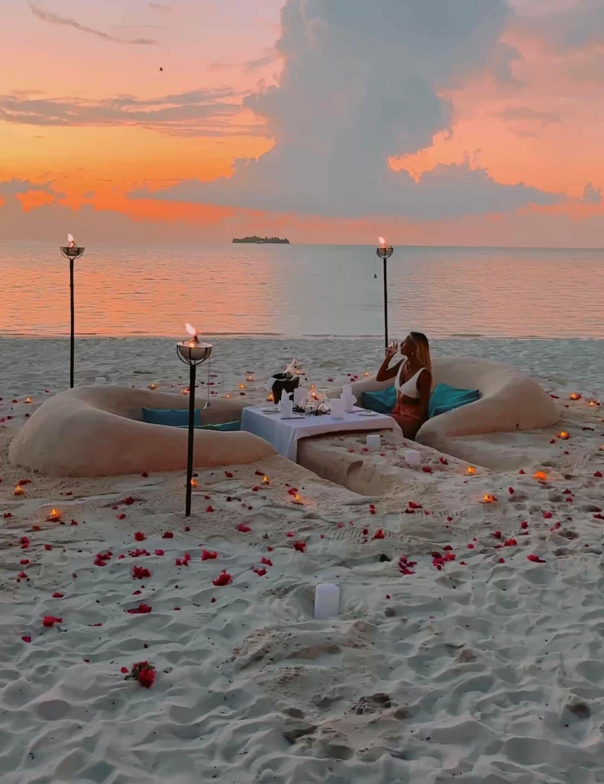 Un entorno de playa con una mesa y sillas, velas y pétalos de rosa.