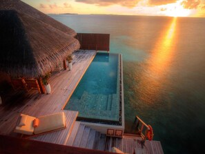 An infinity pool with a wooden deck and a thatched roof structure.