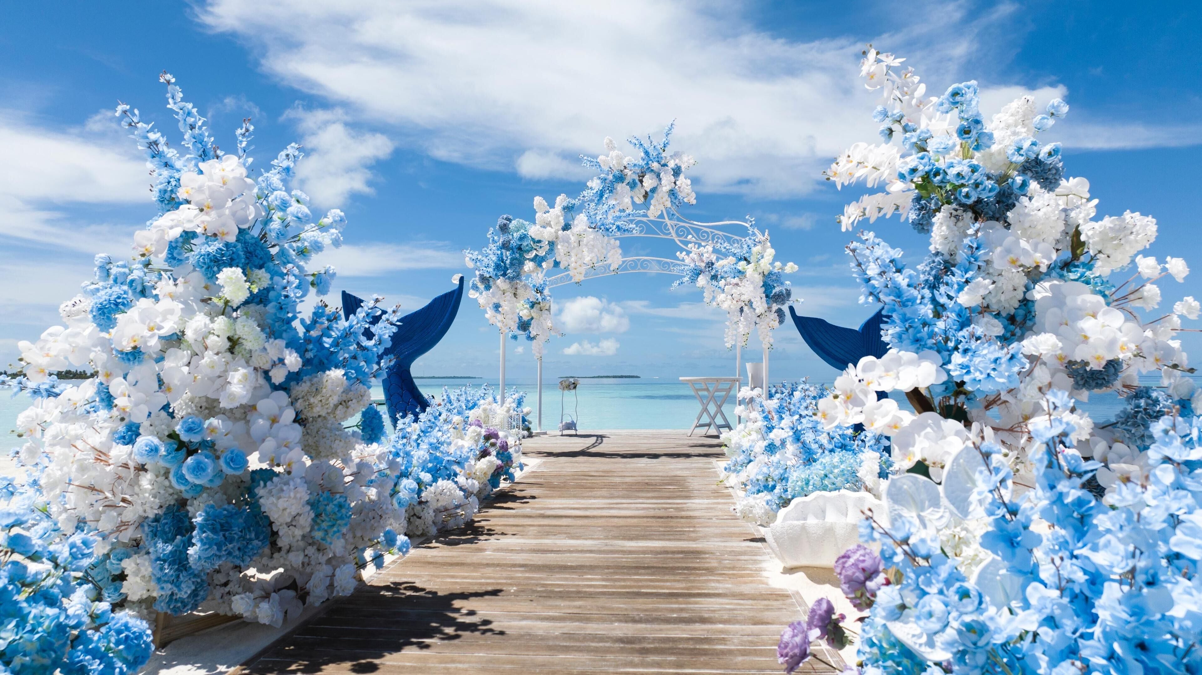 Un sentier en bois mène à une arche ornée de motifs floraux blancs et bleus, d’où l’on a une vue dégagée sur la mer.