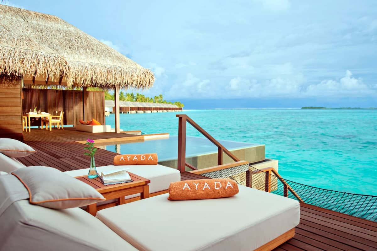 An overwater bungalows with thatched roofs, wooden deck, and a view of the turquoise sea.