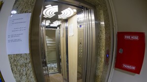 Interior de un ascensor con manguera contra incendios y extintor en la pared, un cartel con instrucciones y una puerta con un número.