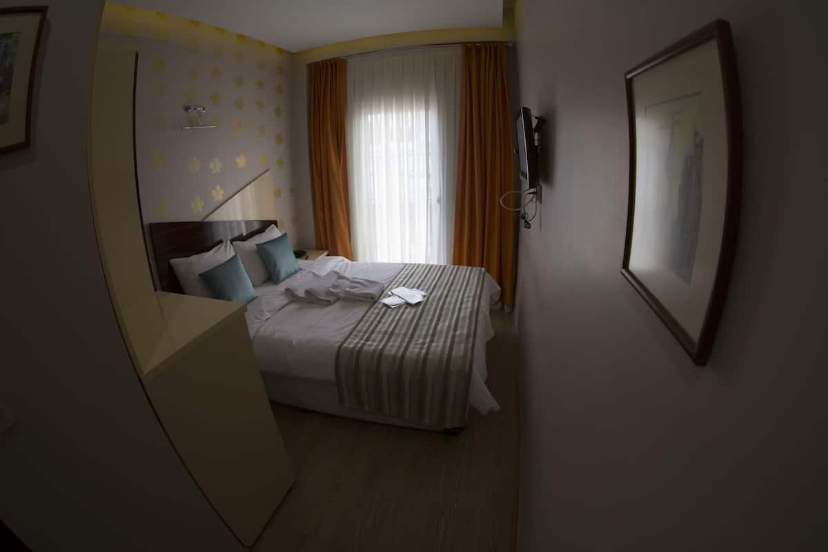 Une chambre d’hôtel avec un lit, un bureau, une chaise, une télévision et une fenêtre avec des rideaux.