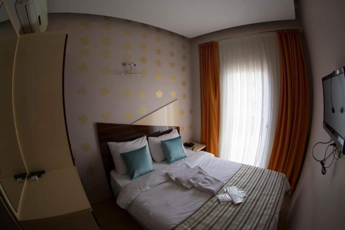 Une chambre d’hôtel avec un mur incurvé, un lit avec une literie blanche et à rayures, des coussins de couleur turquoise et un téléviseur fixé au mur.