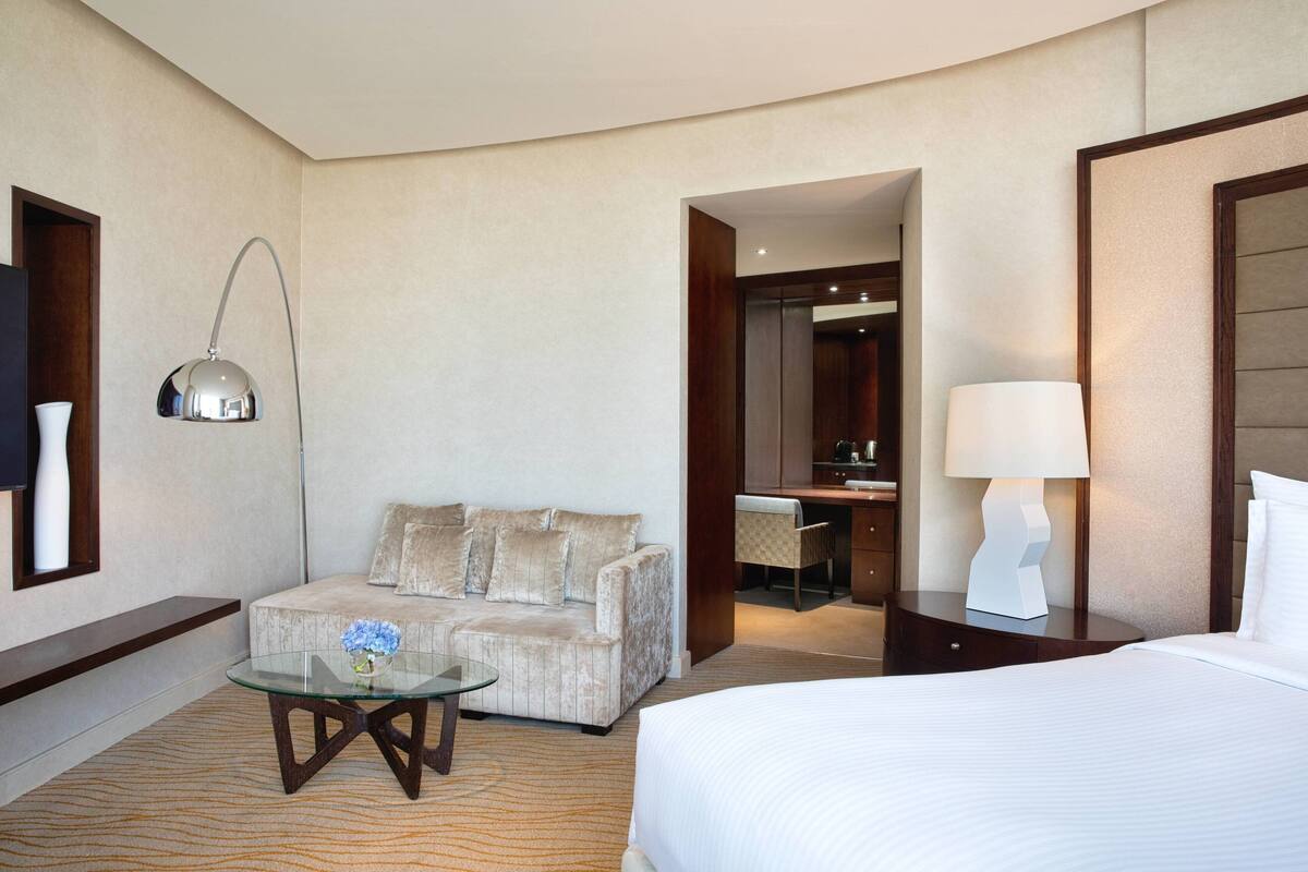 Una habitación de hotel con una cama, un sofá, una mesa de vidrio, una lámpara, un escritorio y una silla.