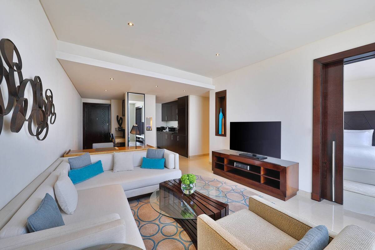 Una sala de estar moderna con un sofá, una mesa de centro y un televisor. Se ve una cocina al fondo.